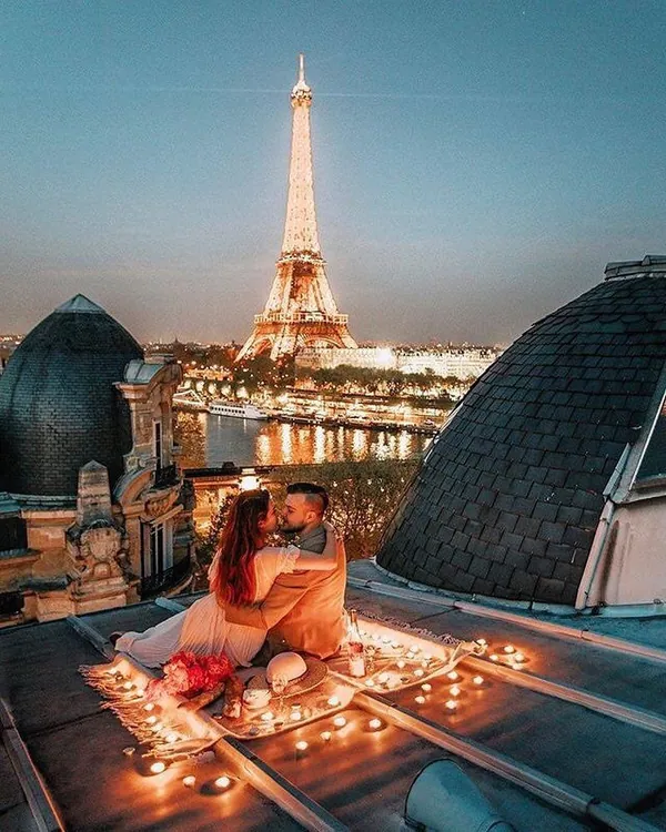 Rooftop Eiffel Romance – Club iLL Repute Couple cuddling on a candle-lit Paris rooftop picnic with the illuminated Eiffel Tower behind them