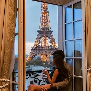 Romantic Eiffel View – Club iLL Repute Couple enjoying champagne by a Paris hotel window overlooking the illuminated Eiffel Tower