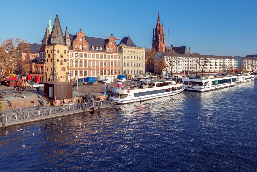 River cruise boats moored along Frankfurt’s Main River, with historic waterfront buildings and Frankfurt Cathedral in the background