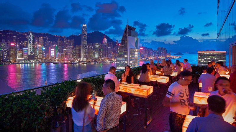Crowd enjoying cocktails at a Hong Kong rooftop bar overlooking Victoria Harbour’s neon skyline at night
